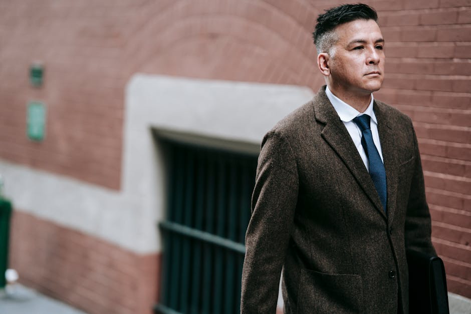 Confident businessman in a suit walking outdoors against a brick wall, exuding professionalism and style.