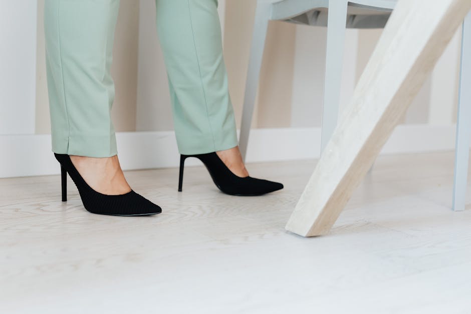 Close-up of elegant black high heels paired with mint green pants on a light wooden floor.
