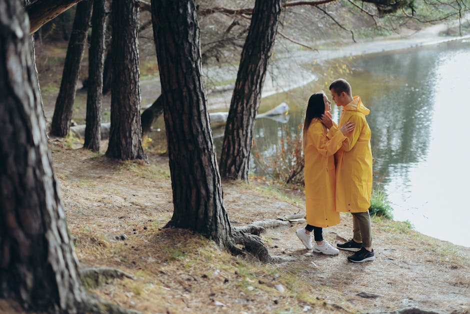 A couple in yellow raincoats sharing a moment in a serene forest by a lake.