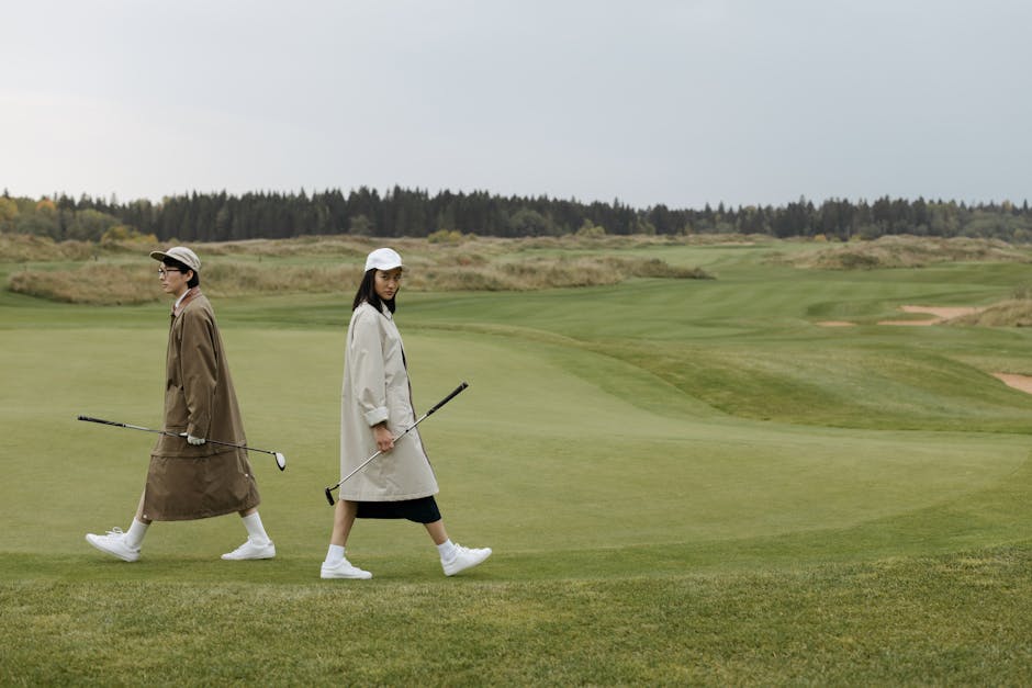 Two fashionable golfers walking across a lush, open golf course, enjoying a leisure day outdoors.